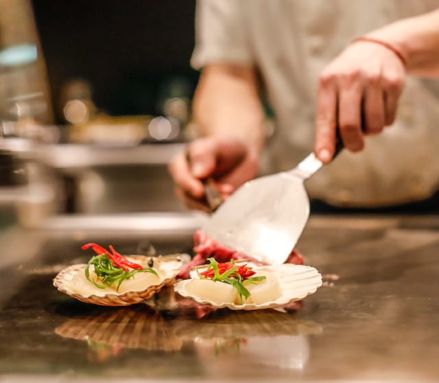 Gasten en kok proosten met wijn aan de teppanyaki-tafel bij restaurant Yuzu in Enschede. Coquille, gril, groepen, bedrijfsuitje, vergadering, zakelijk